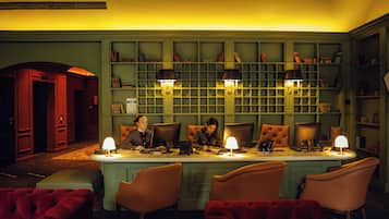 A room with a long table, four chairs, and two lamps. There are bookshelves in the background.