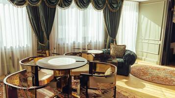 Een goed verlichte woonkamer met een ronde tafel, meerdere stoelen, een bank en een groot raam met gordijnen.