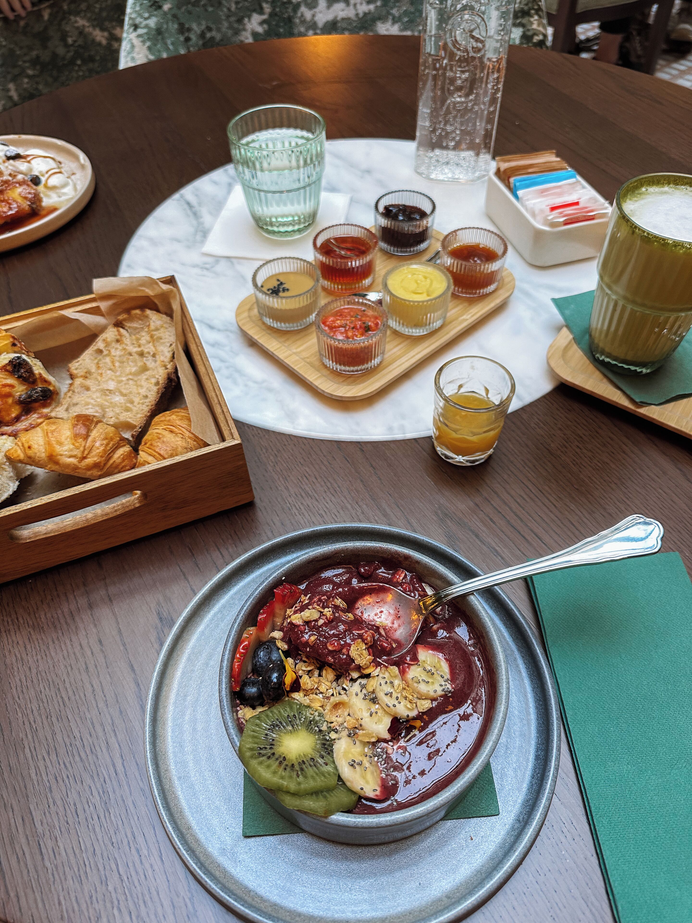 A breakfast setting with a bowl of fruit and granola, a tray of pastries, and small condiment containers.