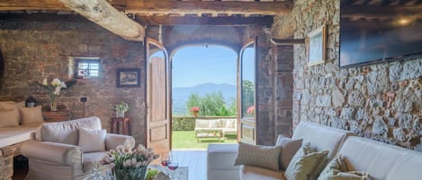 A cozy interior with a stone wall, wooden beams, a sofa, and a view of the outdoors.