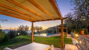 A covered outdoor seating area with a pool, a bed, and a stone wall with lights. - Villa Giannello – Tuscan Hillside Hideaway (Matraia)