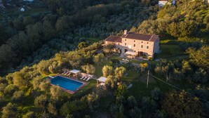 An aerial view of a stone house with a swimming pool, surrounded by dense forest. - Villa Giannello – Tuscan Hillside Hideaway (Matraia)