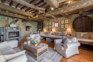 A rustic interior with exposed wooden beams, stone walls, a fireplace, and comfortable seating areas.