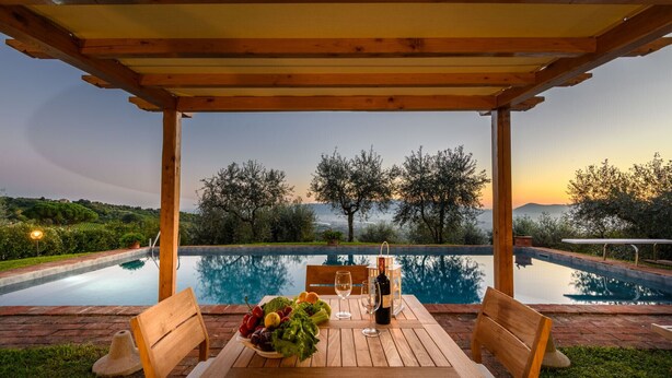 A wooden pergola over a pool with a table set for two, surrounded by greenery and a sunset view. - Villa Giannello – Tuscan Hillside Hideaway (Matraia)