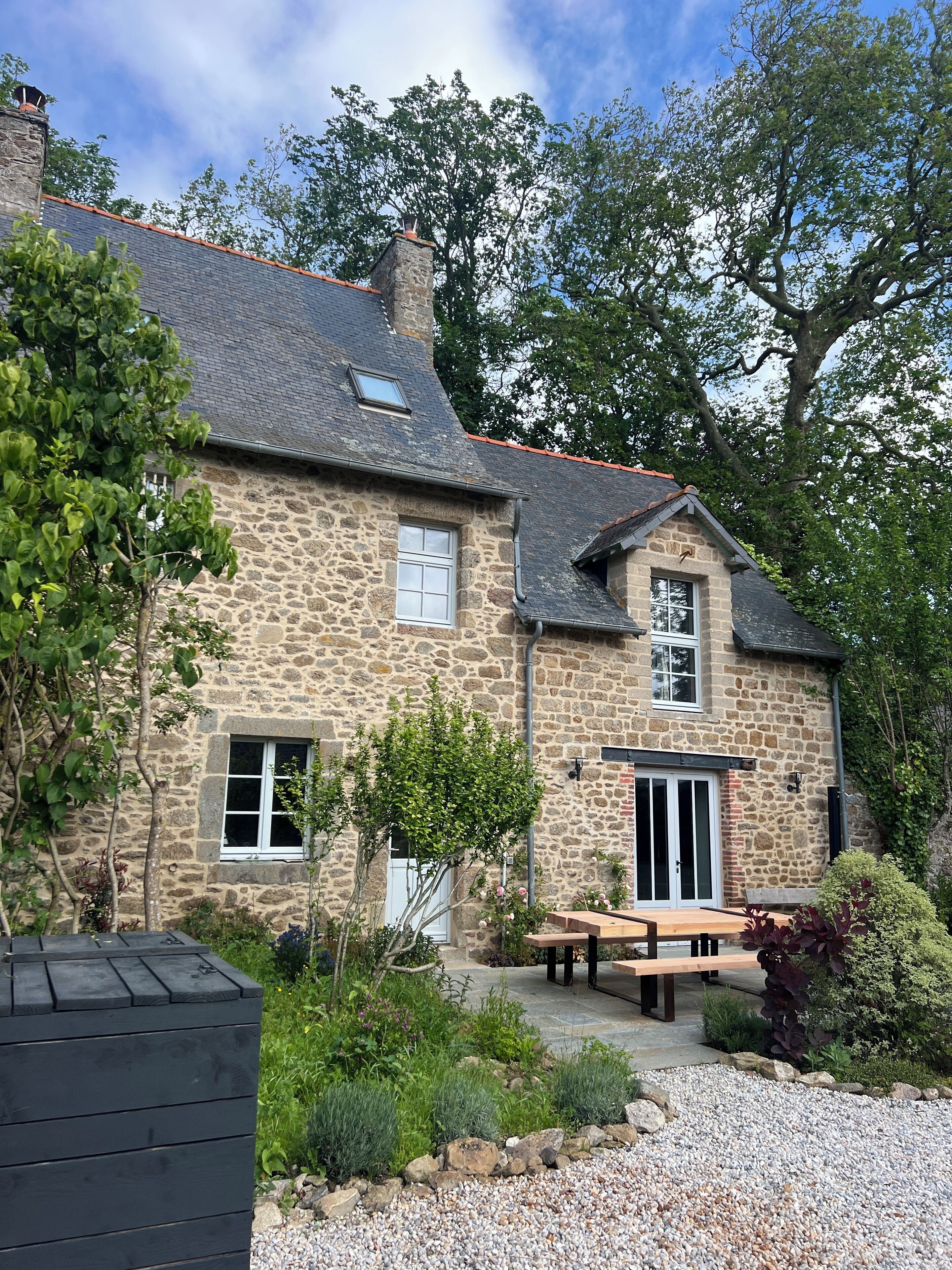 A stone house with a tiled roof, a wooden bench, and a gravel driveway.