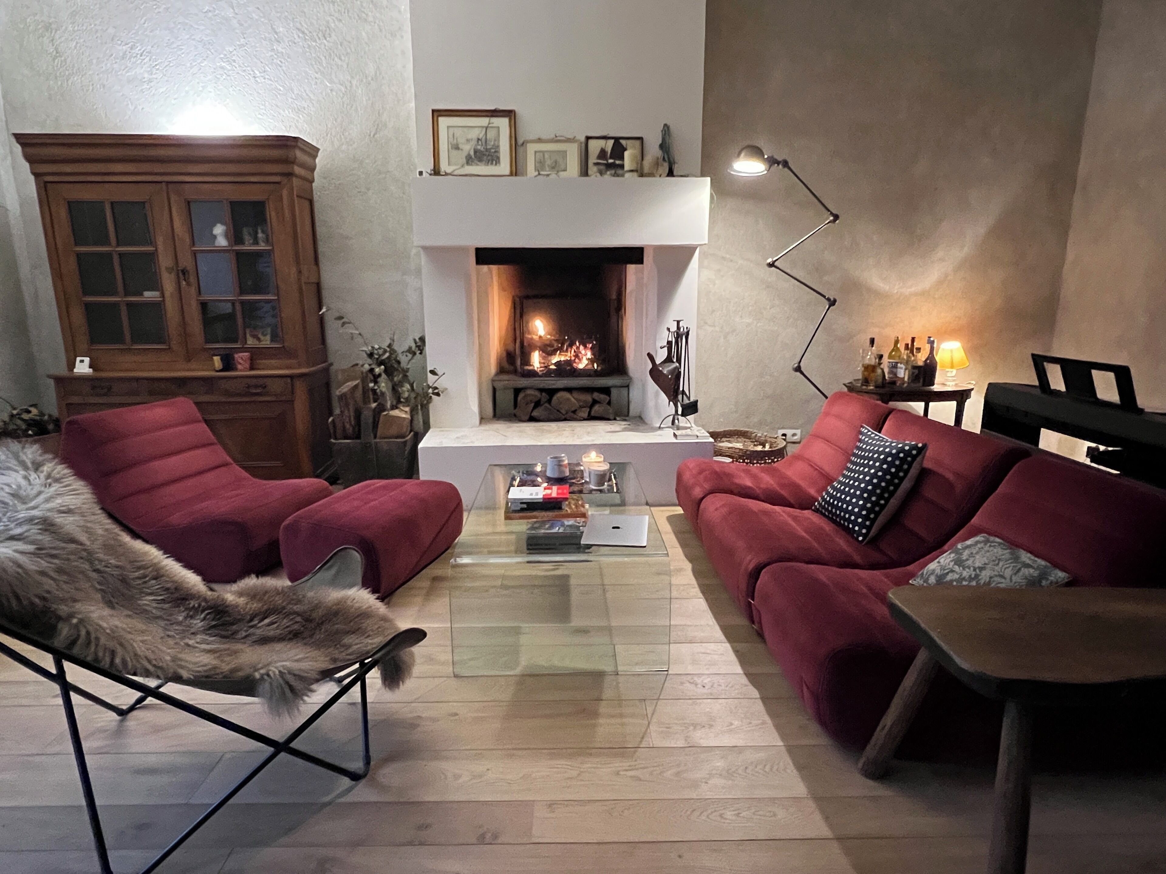 Una sala de estar acogedora con chimenea, sofás rojos, una mesa de centro de vidrio y un armario de madera.