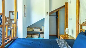 Habitación con cama, cabecera de madera y una escalera que lleva a una zona superior con cestas y una pequeña mesa.