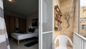 A bedroom with a bed, a wooden wardrobe, and a painting on the wall. - Traditional Maltese 3BD Apartment (Nadur)