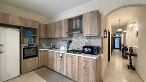 A modern kitchen with wooden cabinets, a built-in oven, a microwave, and a gas stove. - Traditional Maltese 3BD Apartment (Nadur)