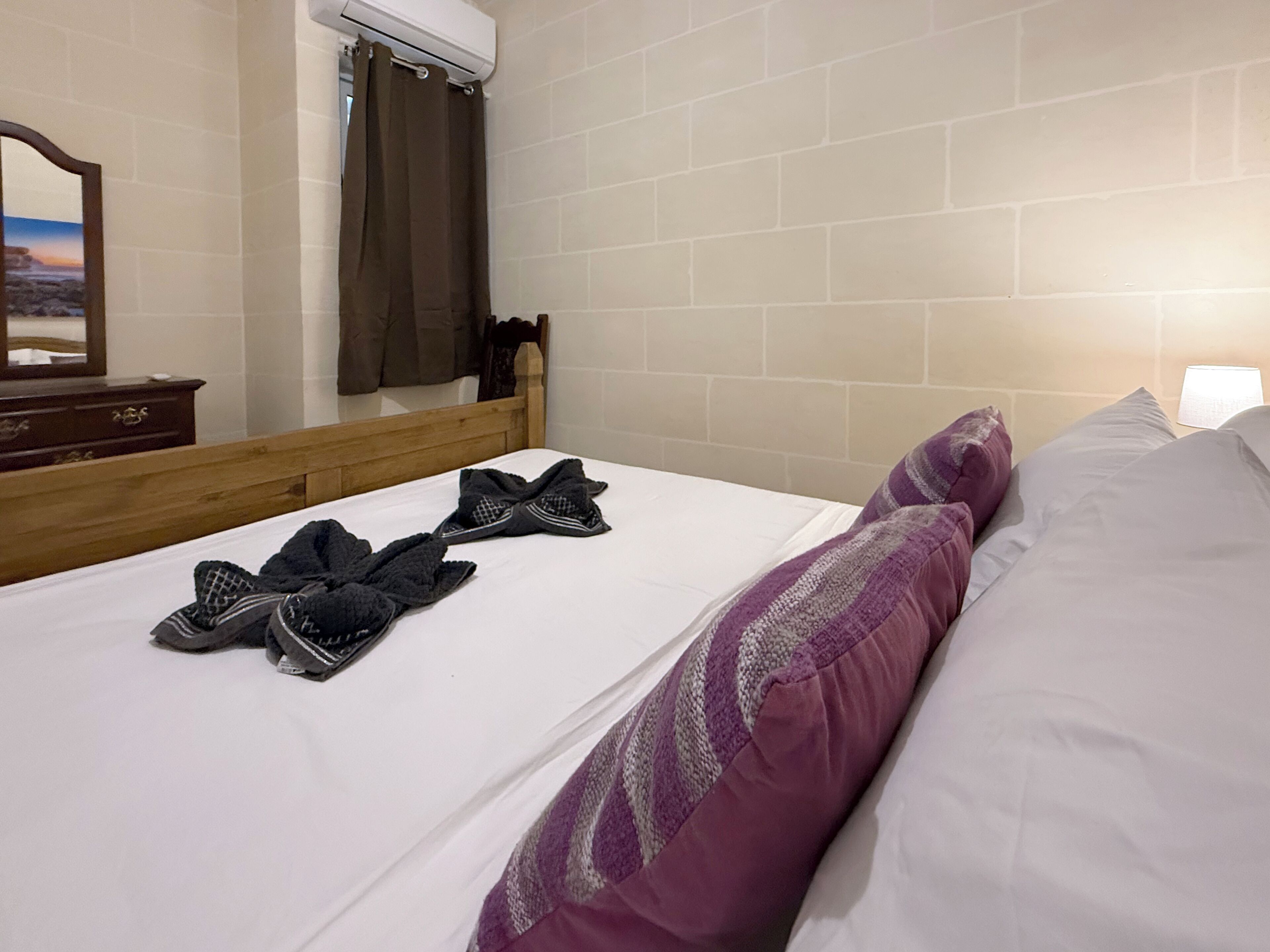 A hotel room with a bed, a wooden headboard, a mirror, and a window with a curtain.