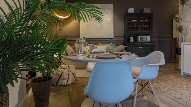 A modern living room with a round dining table, blue chairs, a sofa, and a cabinet with kitchen appliances.