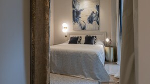 A bedroom with a bed, a nightstand, a wall-mounted light, and a painting.