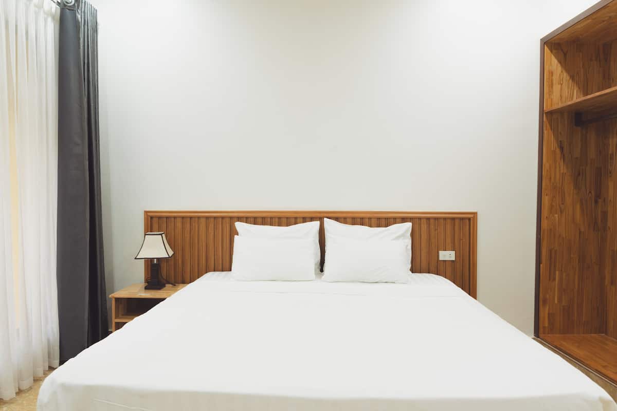A neatly made bed in a room with a wooden headboard, a nightstand with a lamp, and a wooden shelf.