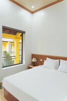 Habitación de hotel con una cama, una mesita de noche, una lámpara, un ventanal con vista a un espacio exterior y un techo de madera.
