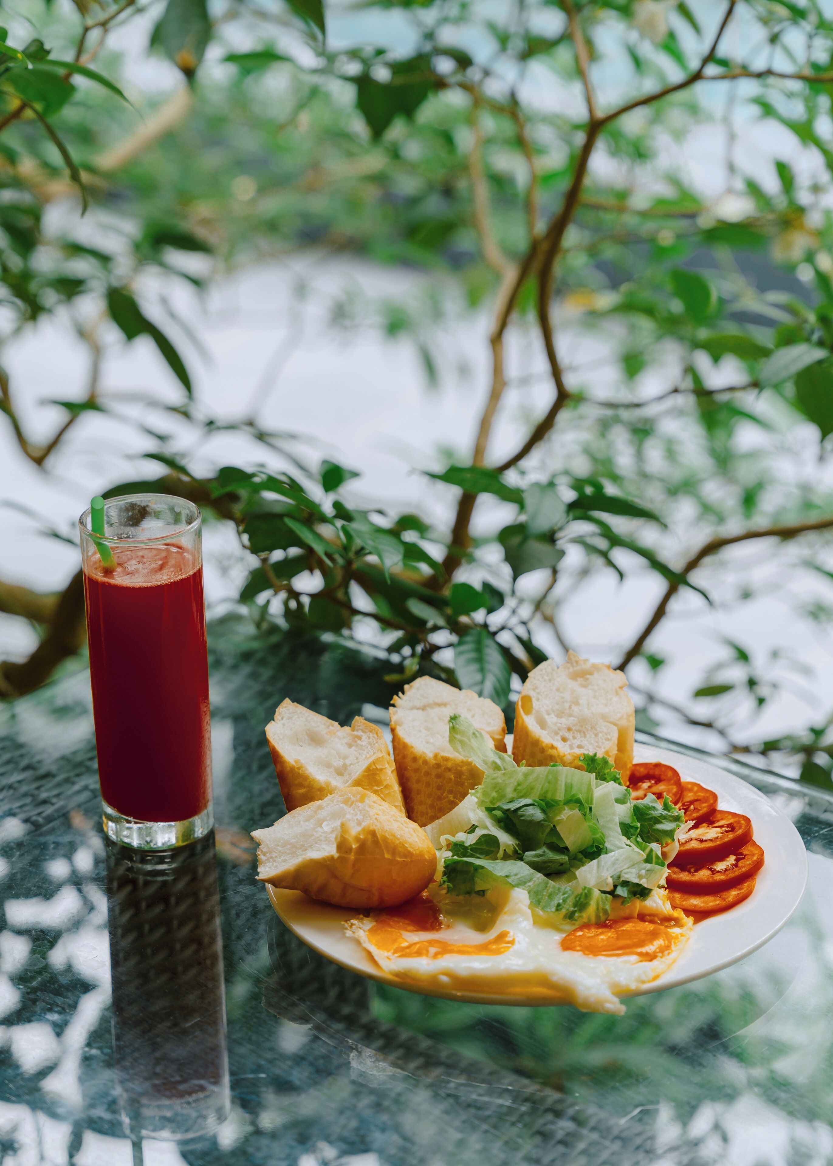 Un verre de jus de fruits rouge, du pain, une salade et des tomates sur une table, avec un verre d’eau.