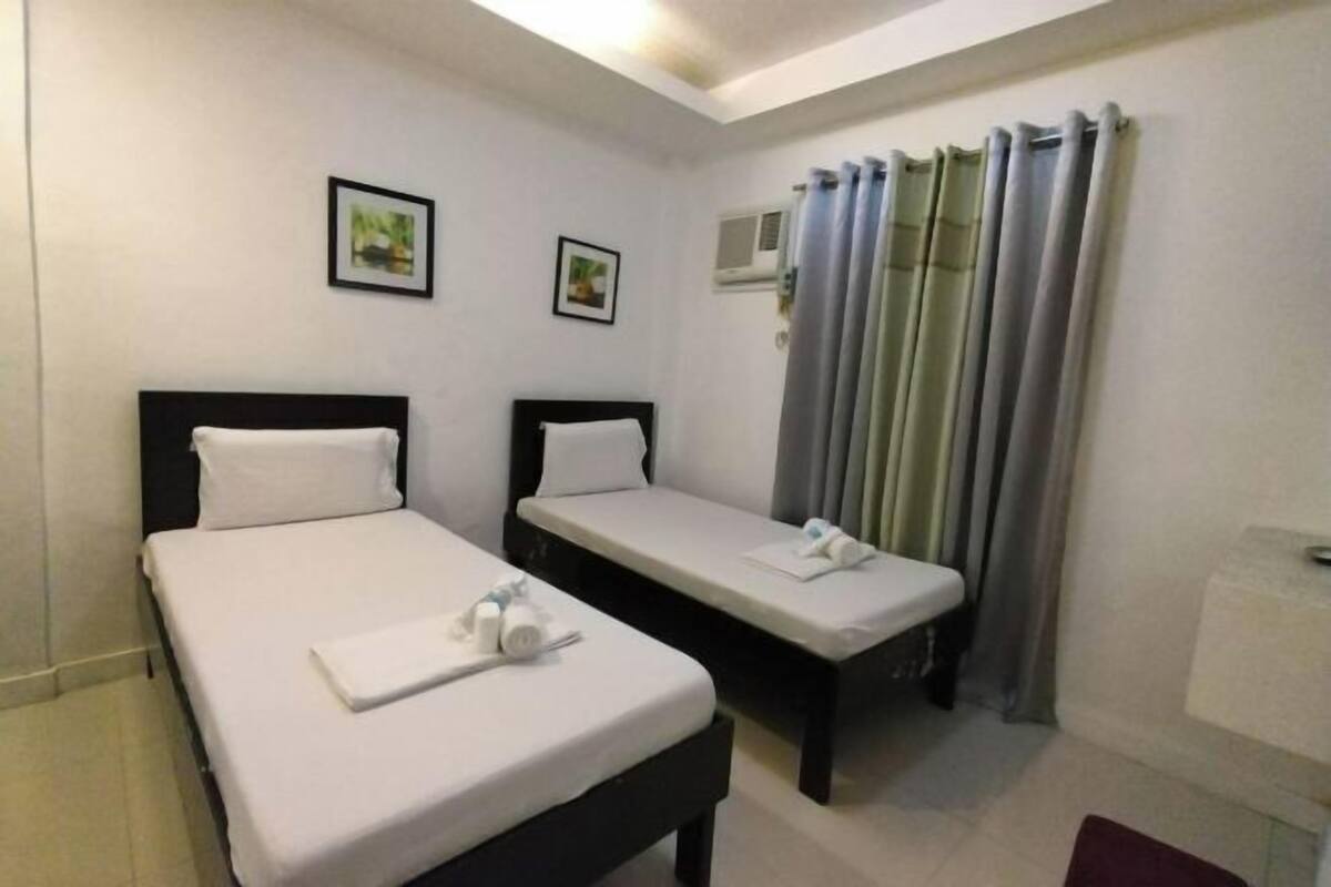 A hotel room with two single beds, a small table, a mirror, and a window with curtains.