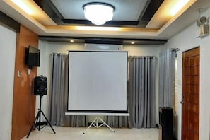 A conference room with a projector screen, curtains, a speaker, and a ceiling light fixture. - LIVEWIRE PLANET SUITES (General Santos)