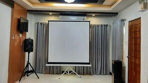 A conference room with a large projection screen, curtains, a speaker on a tripod, and a chandelier. - LIVEWIRE PLANET SUITES (General Santos)