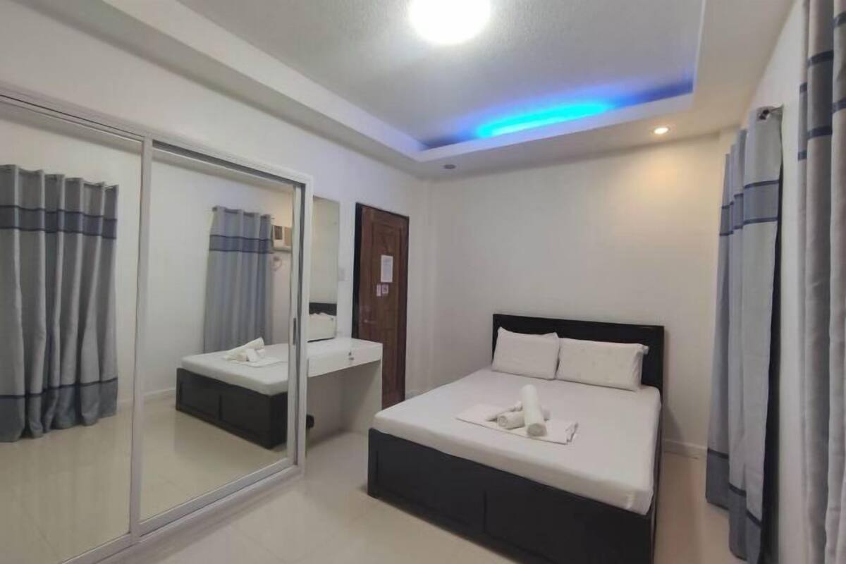 A hotel room with a bed, bedside table, and a mirror.
