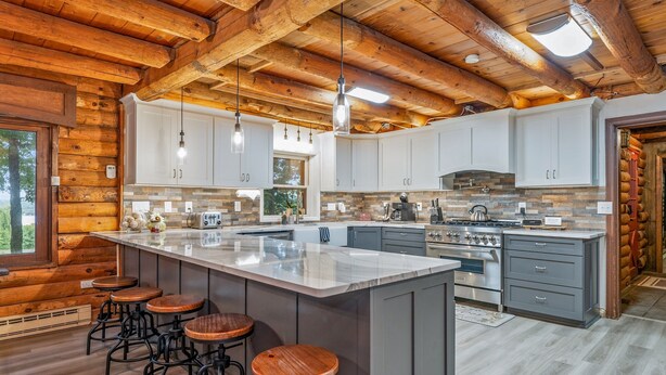 A spacious kitchen with a large island, wooden ceiling beams, and bar stools. - Canandaigua Cabin Retreat | Lake Views | Hot Tub (Canandaigua)