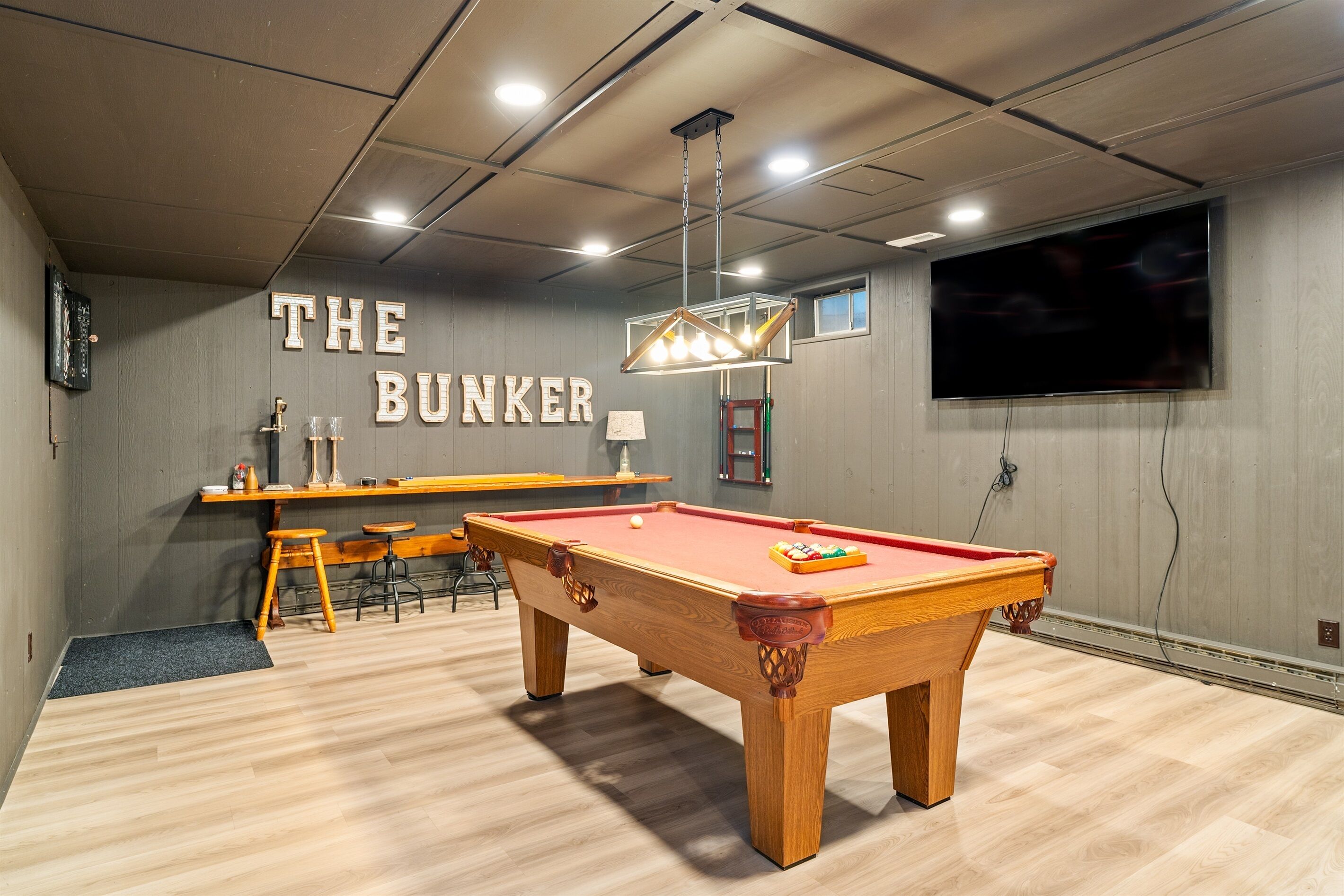 Een pooltafel met een rode viltkleed, een houten bar met krukken en een aan de muur bevestigde televisie.