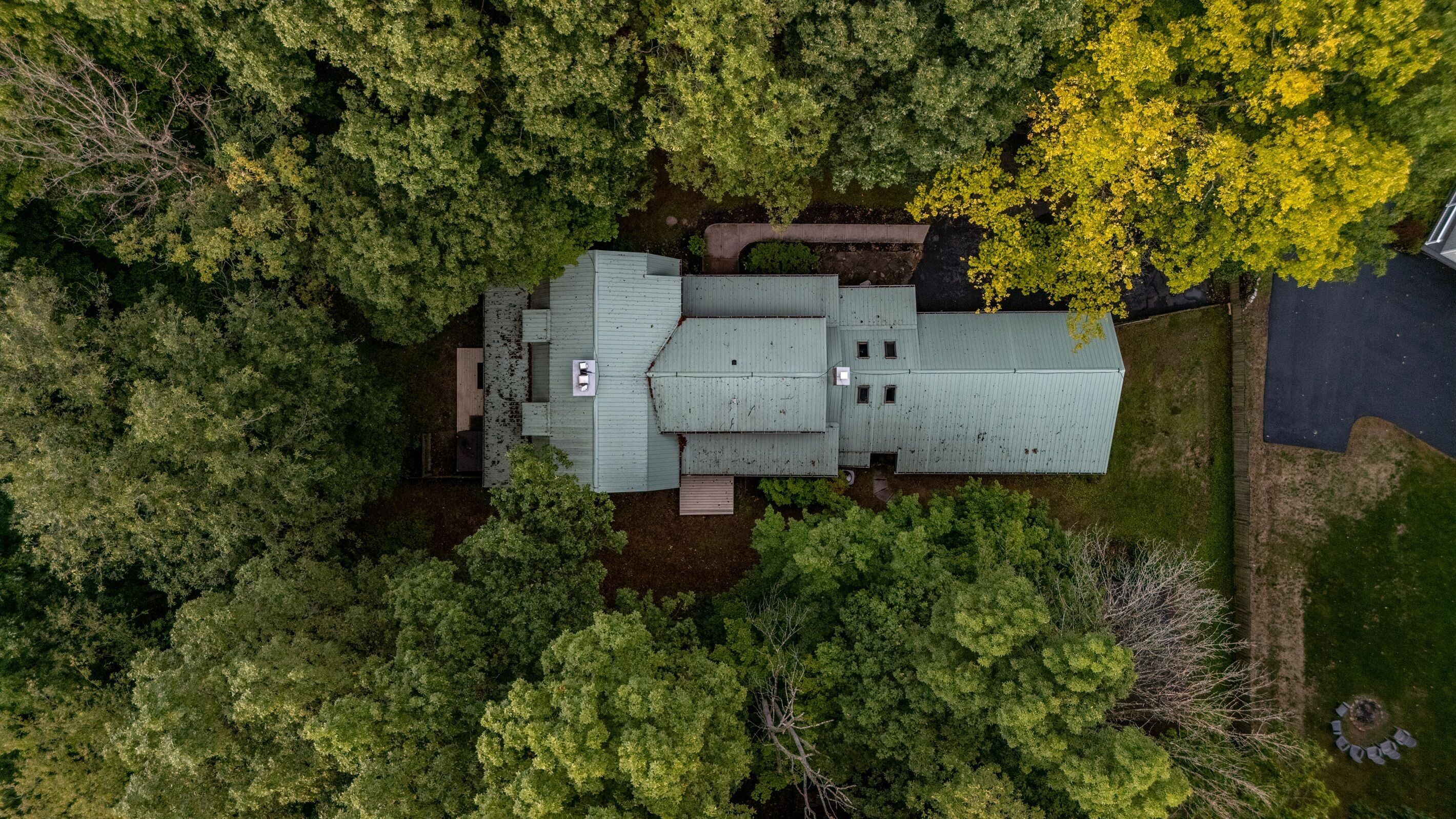 Luchtbeeld van een gebouw met twee verdiepingen, omringd door dichte bomen, met een zichtbare oprit en een kleine tuin.