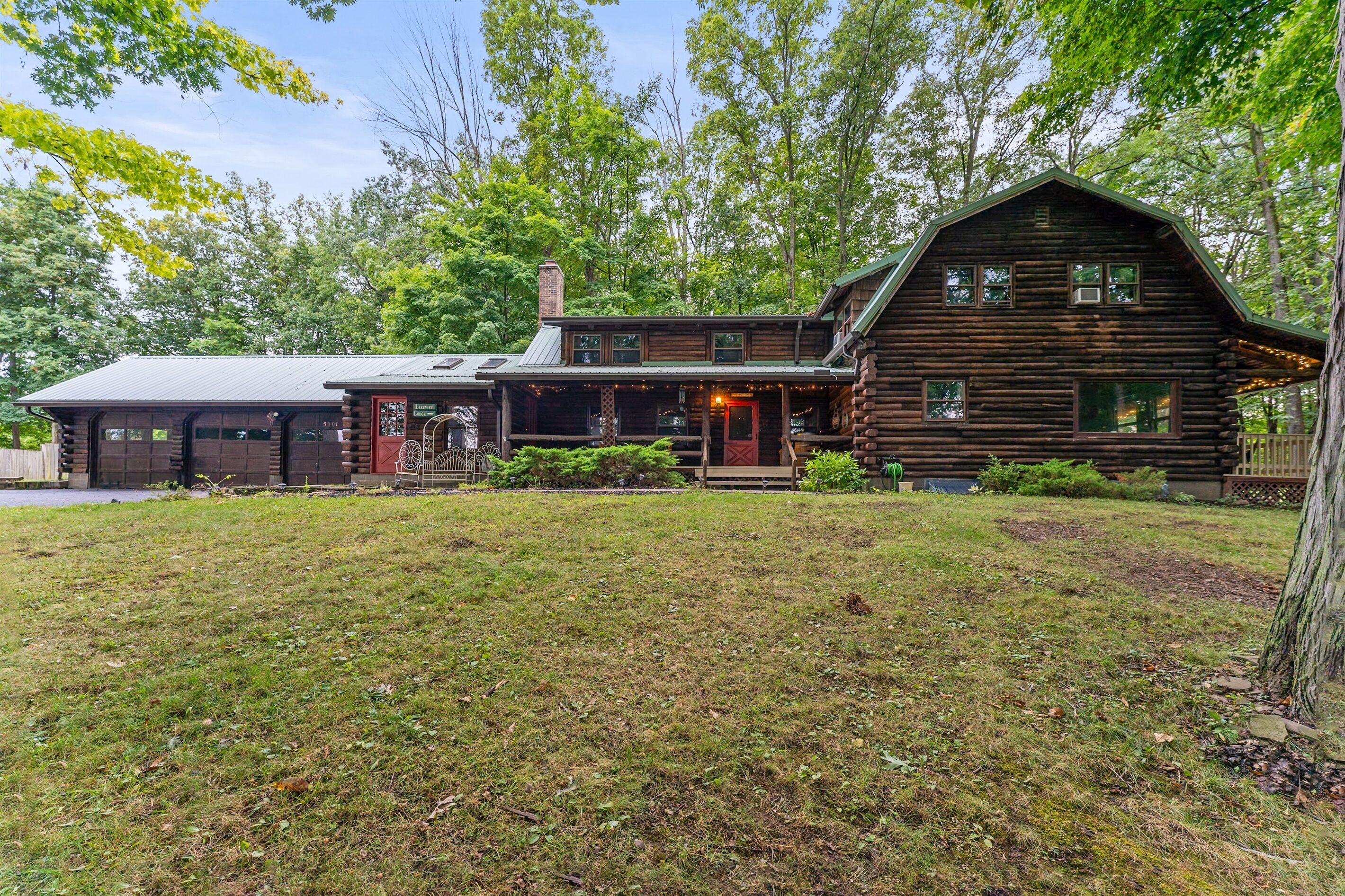 A rustic log cabin with a front porch, a garage, and a large yard.