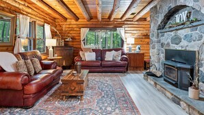 A log cabin interior with a stone fireplace, leather sofas, and a rustic wooden ceiling. - Canandaigua Cabin Retreat | Lake Views | Hot Tub (Canandaigua)