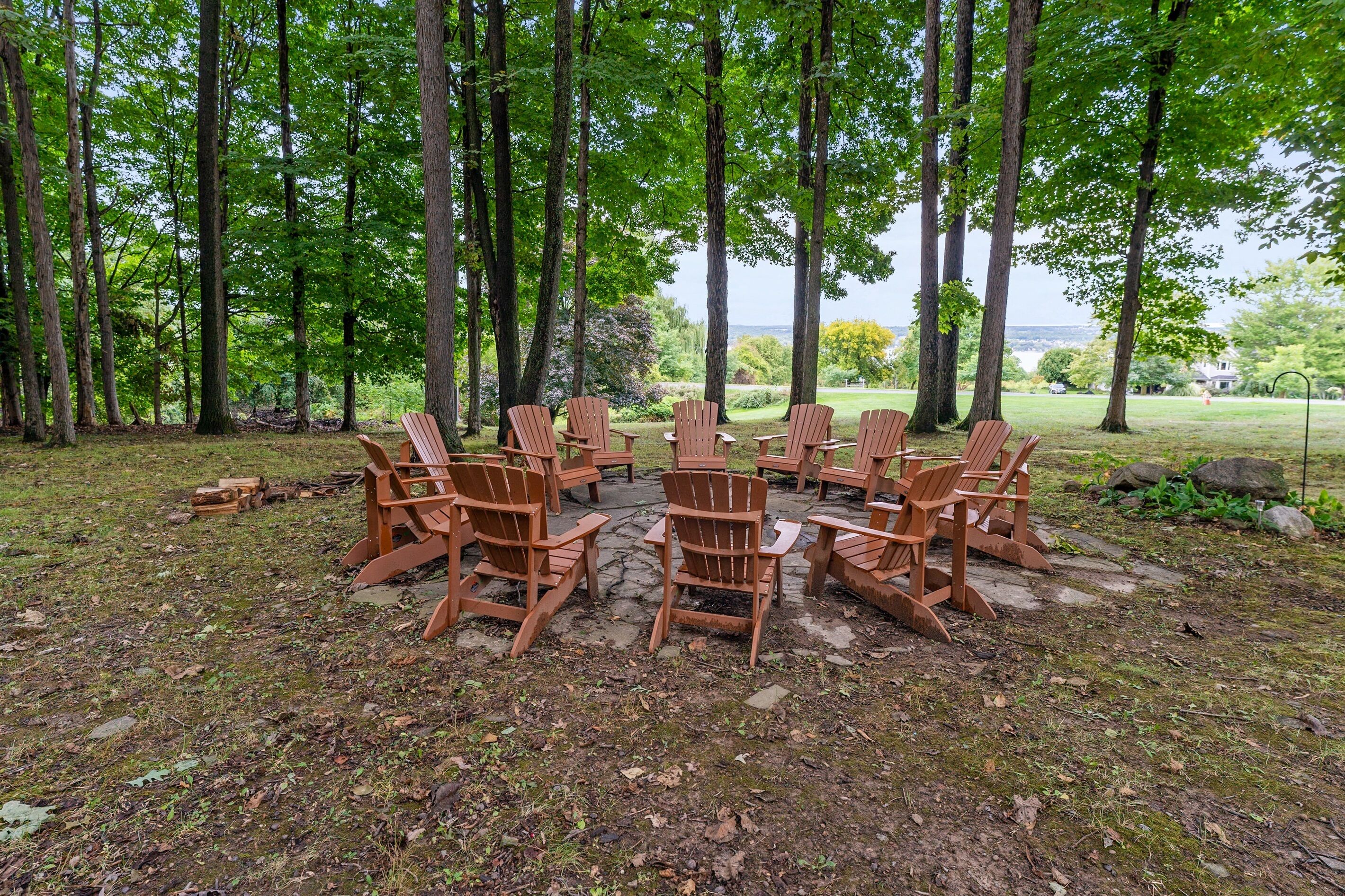Een cirkelvormige opstelling van houten Adirondack-stoelen in een bosrijk gebied, met uitzicht op een waterpartij.