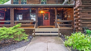 A rustic log cabin with a porch, wooden steps, and a red door. - Canandaigua Cabin Retreat | Lake Views | Hot Tub (Canandaigua)