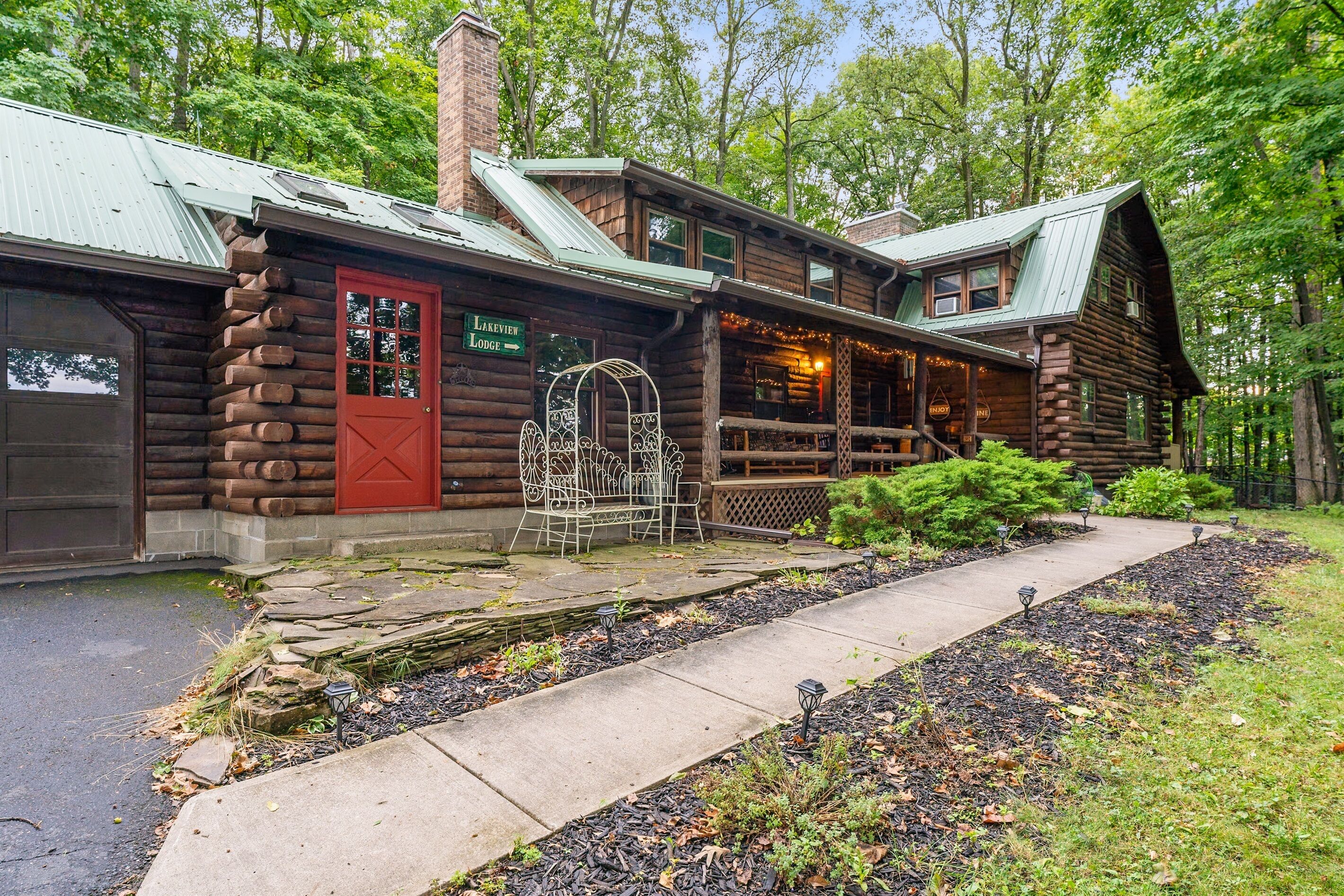 A log cabin with a red door, a covered porch, and a stone pathway leading to the entrance.