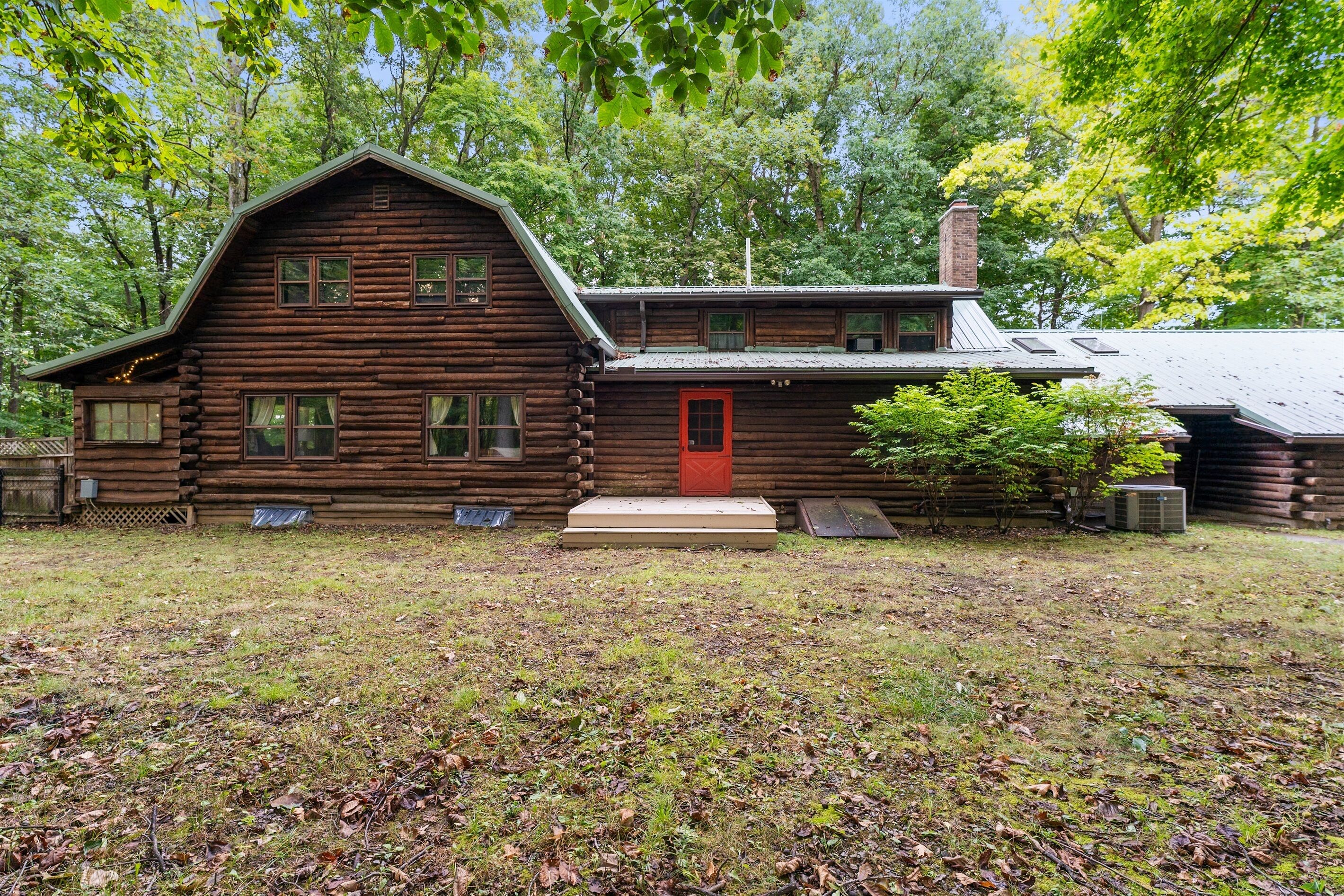 A rustic log cabin with a red door, a chimney, and a small porch area.