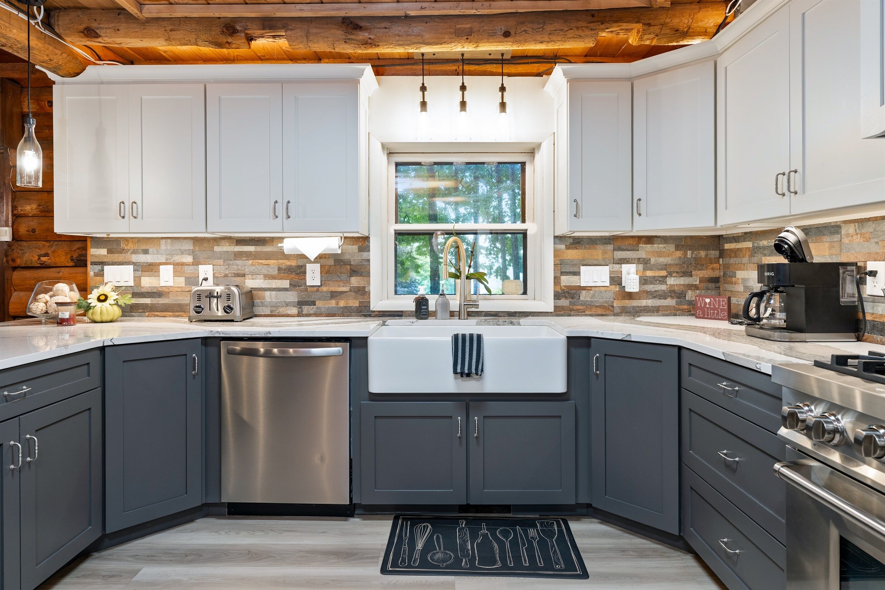 A modern kitchen with grey cabinets, a stainless steel dishwasher, a built-in oven, and a window above the sink.