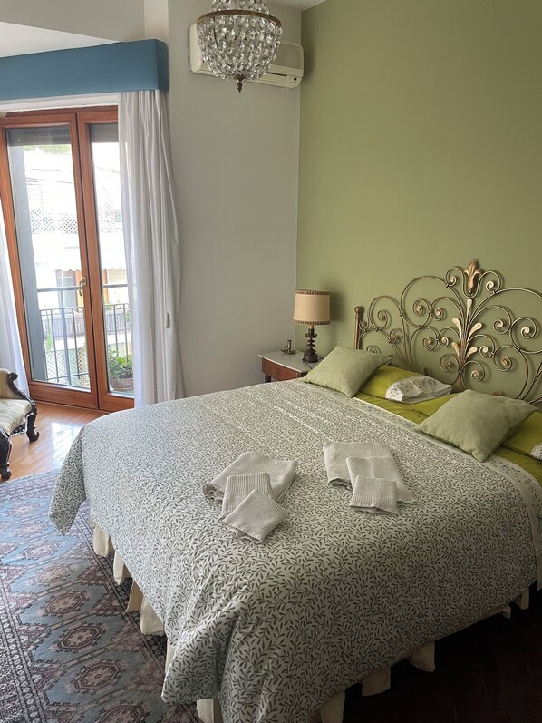A neatly made bed with a patterned bedspread and pillows, a chandelier, and a view of the outdoors through a sliding glass door. - Panoramic at Posillipo (Napoli)
