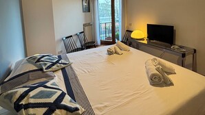 Quarto de hotel com uma cama grande, uma escrivaninha com computador, televisão e varanda com vista.