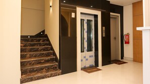 A modern elevator with glass panels and a fire extinguisher mounted on the wall. - The Maheshwar Hotel (Varanasi)