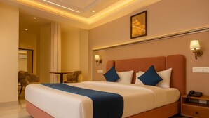 A hotel room with a large bed, two bedside tables, a nightstand, a chair, and a framed picture on the wall. - The Maheshwar Hotel (Varanasi)