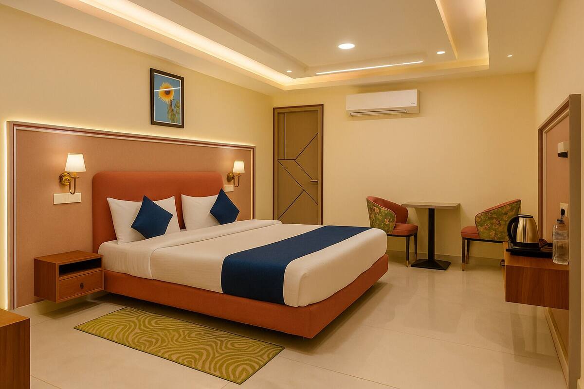 A hotel room with a large bed, bedside tables, a desk, two chairs, an air conditioning unit, and a framed picture on the wall.
