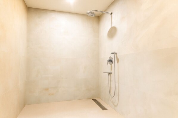 A small, empty shower room with a single showerhead and a handheld shower attachment.