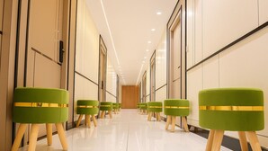 A hallway with green upholstered chairs with wooden legs and gold accents, leading to a door at the end. - The Maheshwar Hotel (Varanasi)