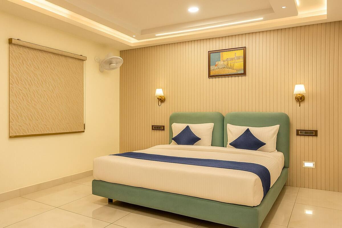 A modern hotel room with a large bed, two wall-mounted lights, a ceiling fan, and a painting on the wall.