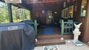 A wooden cabin with a covered porch, a welcome mat, and a statue.