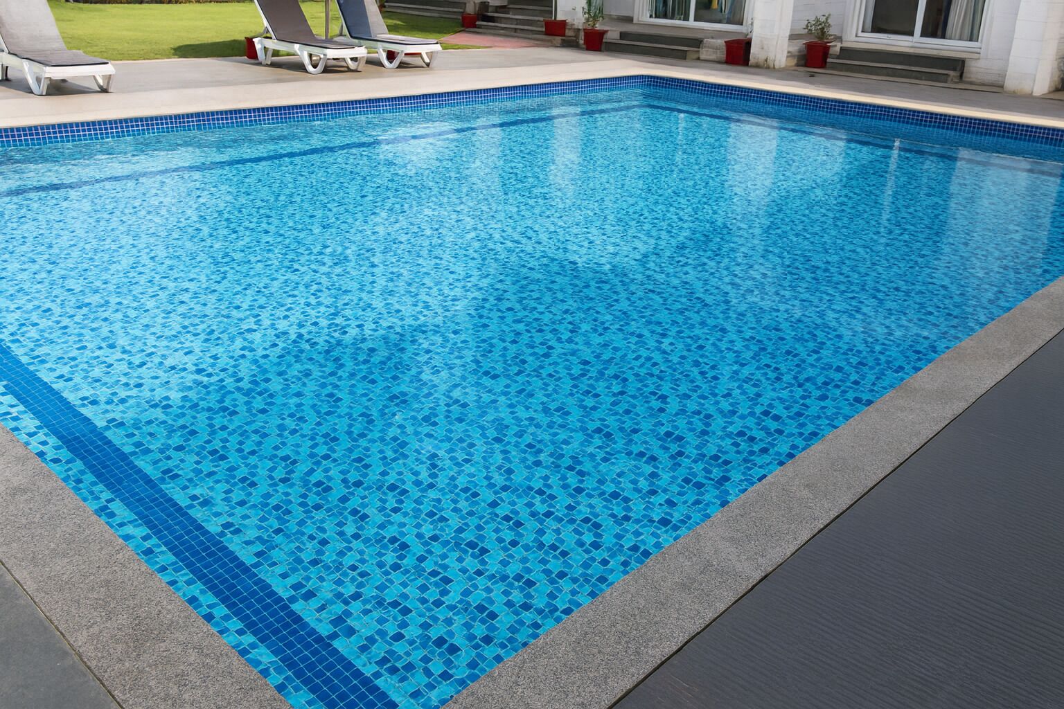 A rectangular swimming pool with blue mosaic tiles and a dark grey border.
