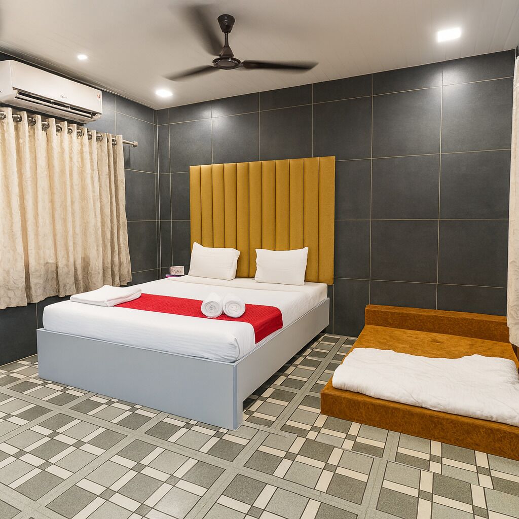 A modern hotel room with a large bed, a smaller sofa, a ceiling fan, and a tiled floor.