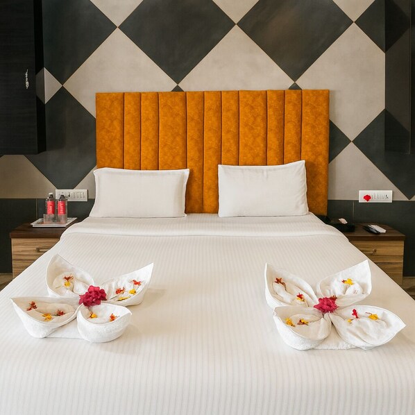 A hotel room with a large bed, two pillows, a headboard, and a nightstand with a phone and a bottle.