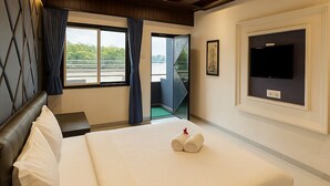 A hotel room with a large bed, a TV mounted on the wall, and a view of the outdoors through the window. - River Splash Resort Neral Karjat (Karjat)