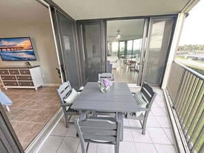 A balcony with a table and chairs, a TV on the wall, and a view of the outside.
