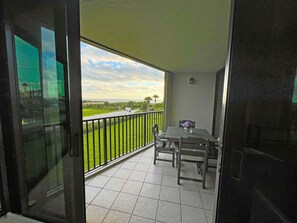 Ein Balkon mit Tisch und Stühlen, Blick auf eine grüne Landschaft und einen klaren Himmel.