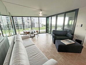 Een moderne woonkamer met een bank, een salontafel en een balkon met uitzicht op gebouwen en groen.