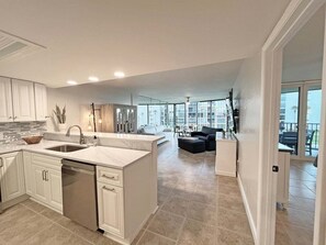 A modern kitchen with a large island, a dining area with a sofa, and a view through large windows.